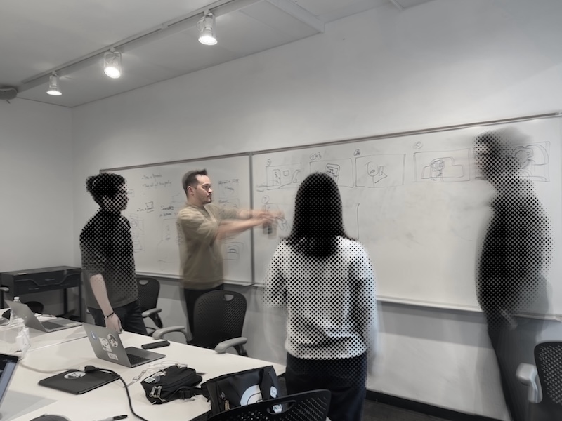 Photo of Max explaining an idea while pointing at a storyboard drawn on a white board in front of his team