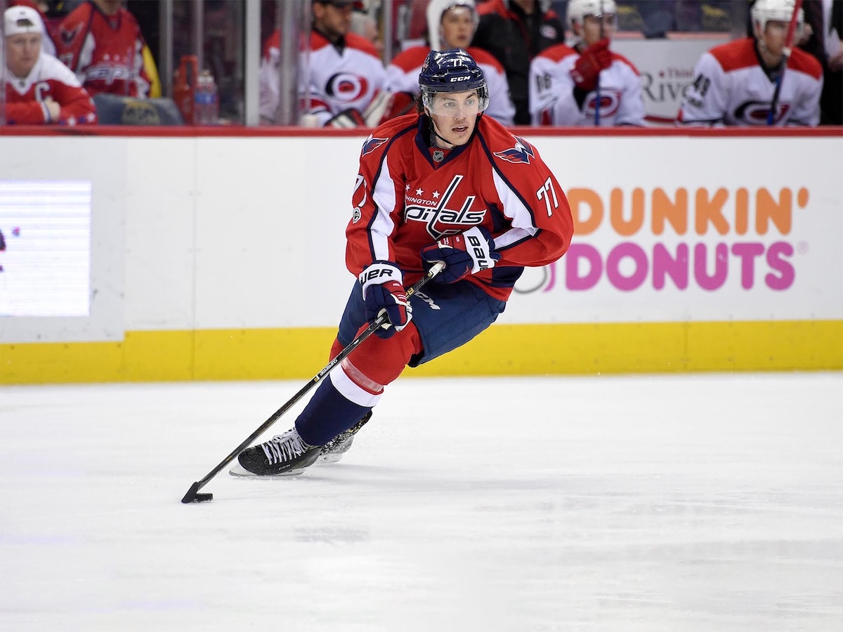 A photo of #77, T.J. Oshie, aggressively skating down the ice with his stick outstretched, looking to the side for his teammate to pass to him.